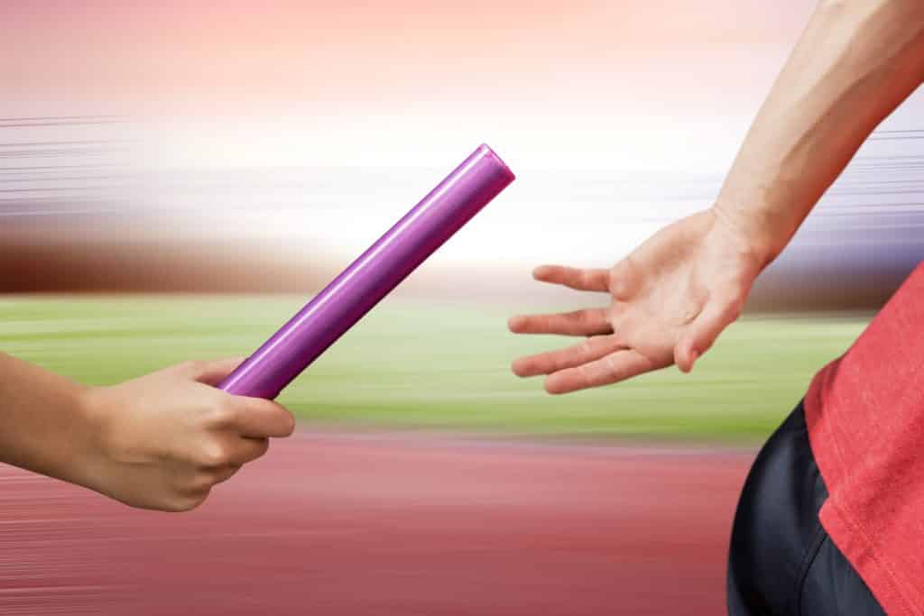 hand passing a violet baton to the another person's hand while running