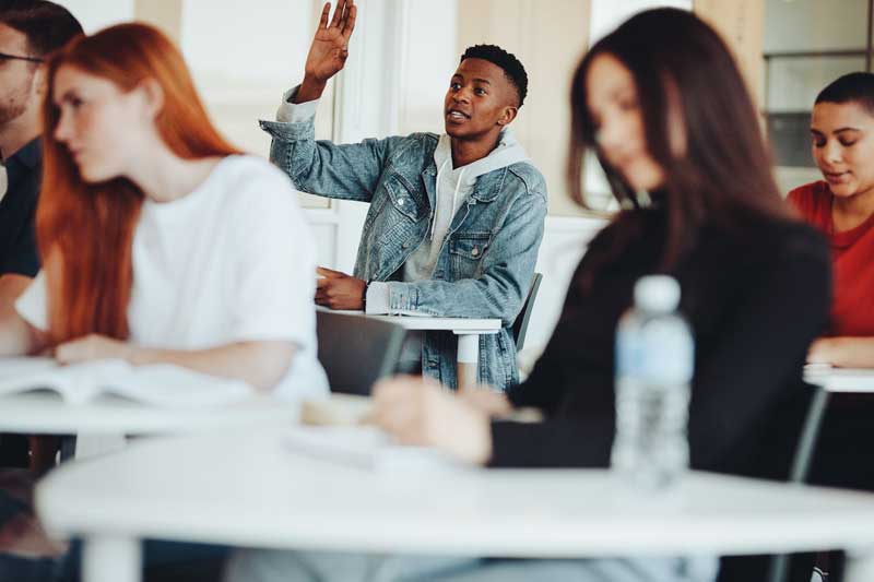 male student in classroom with hand raised