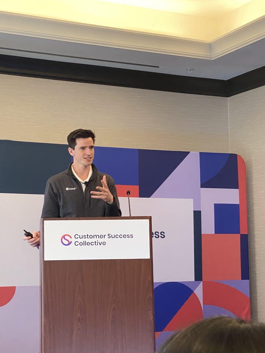 harris clarke speaking on a stage at a customer success collective event with a presentation