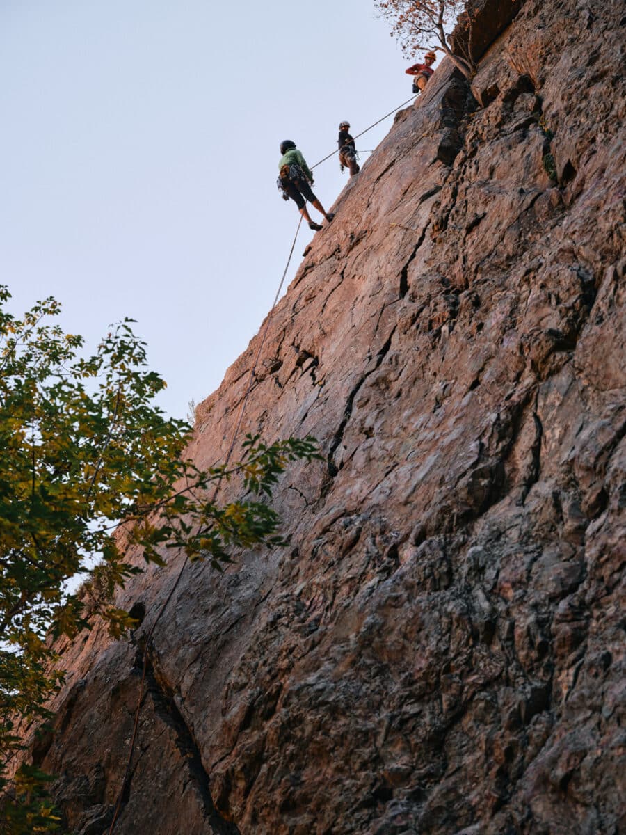 three people rapelling on a rocky cliff