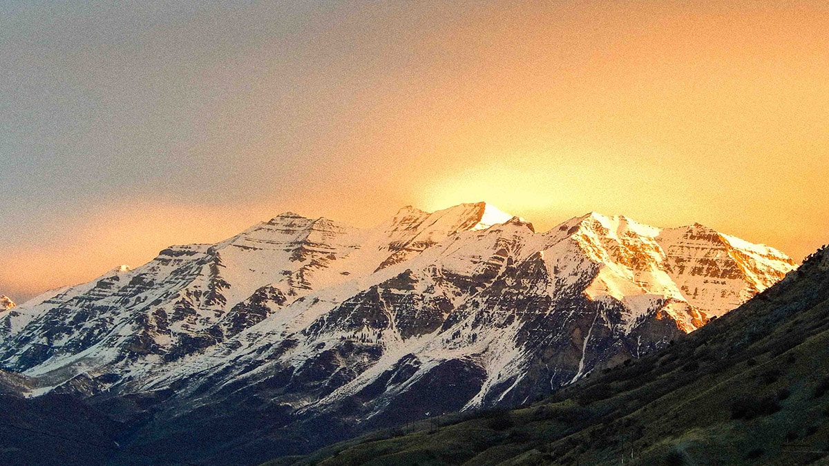 snow covered mountain being lit up by a sunrise