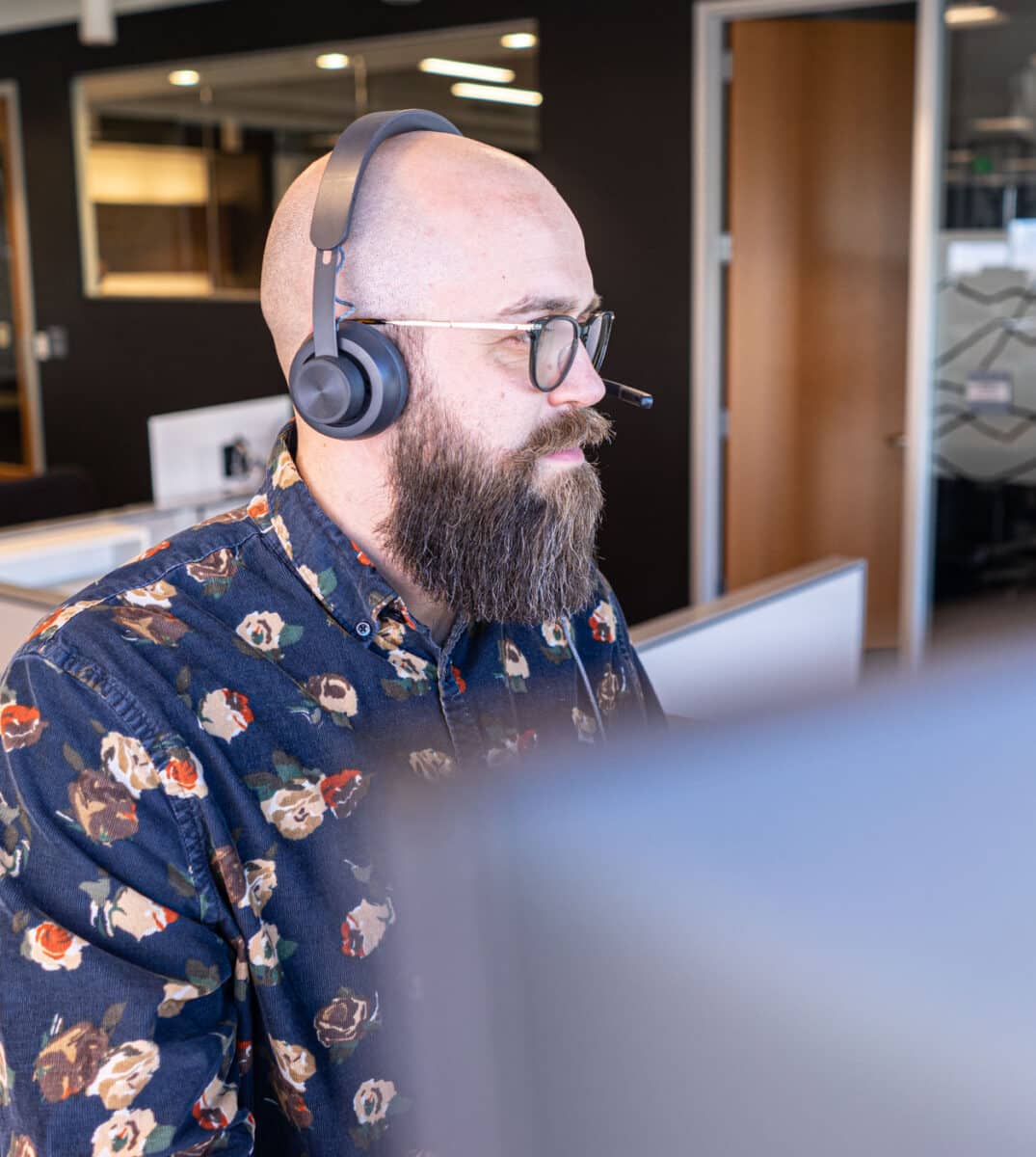 white bald man with a beard looking at a computer working with a headset on