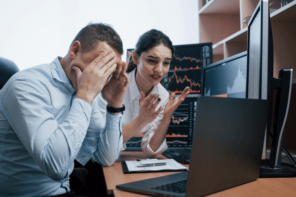 A man and woman sitting at a desk and looking frustrated.