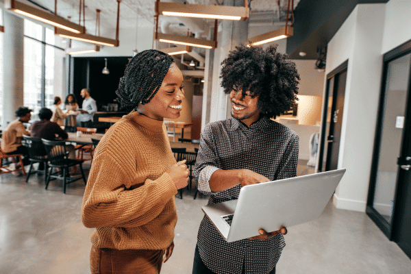 A man and a woman standing in an office, looking at a laptop.