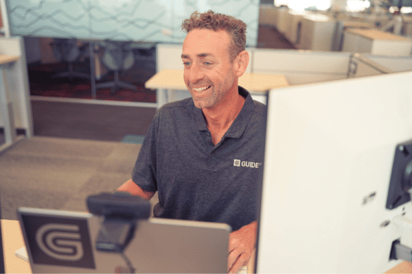 Man with a GUIDEcx polo shirt, sitting at a computer.