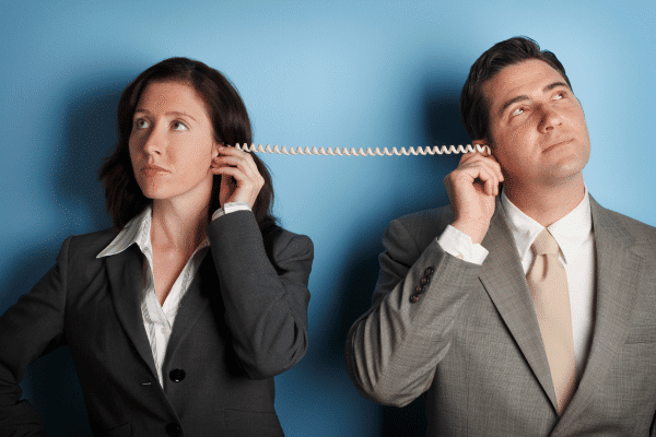 A man and a woman dressed in business suits, holding a telephone cord between their ears. 
