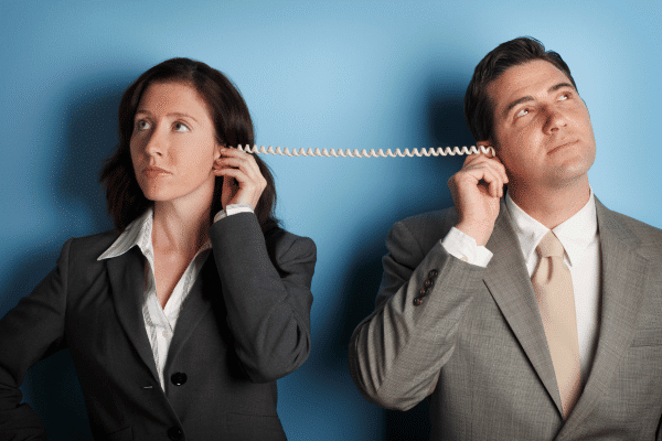 A man and a woman dressed in business suits, holding a telephone cord between their ears.